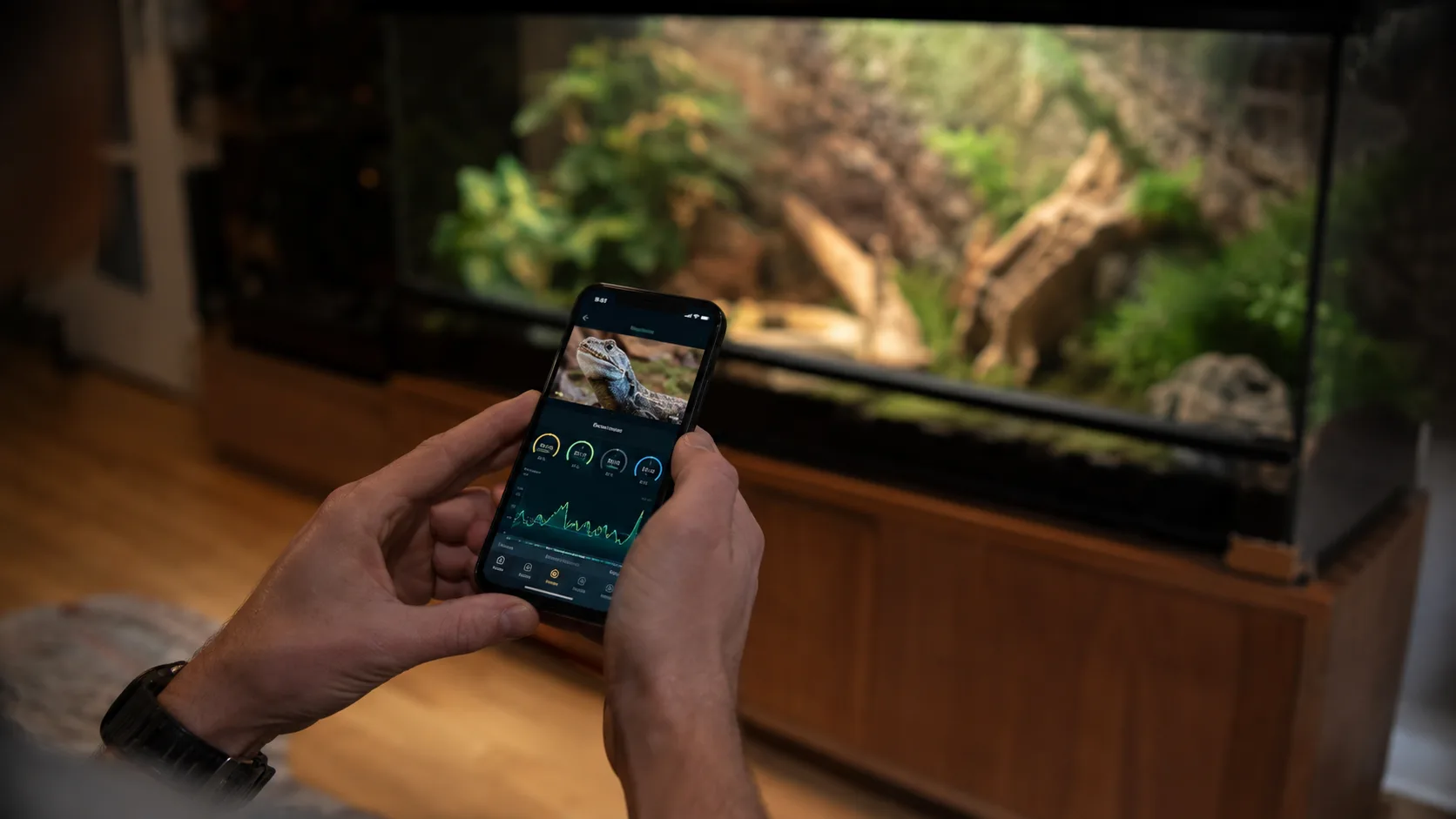 A person checking a reptile-care app on their phone beside a well-set-up bioactive terrarium.