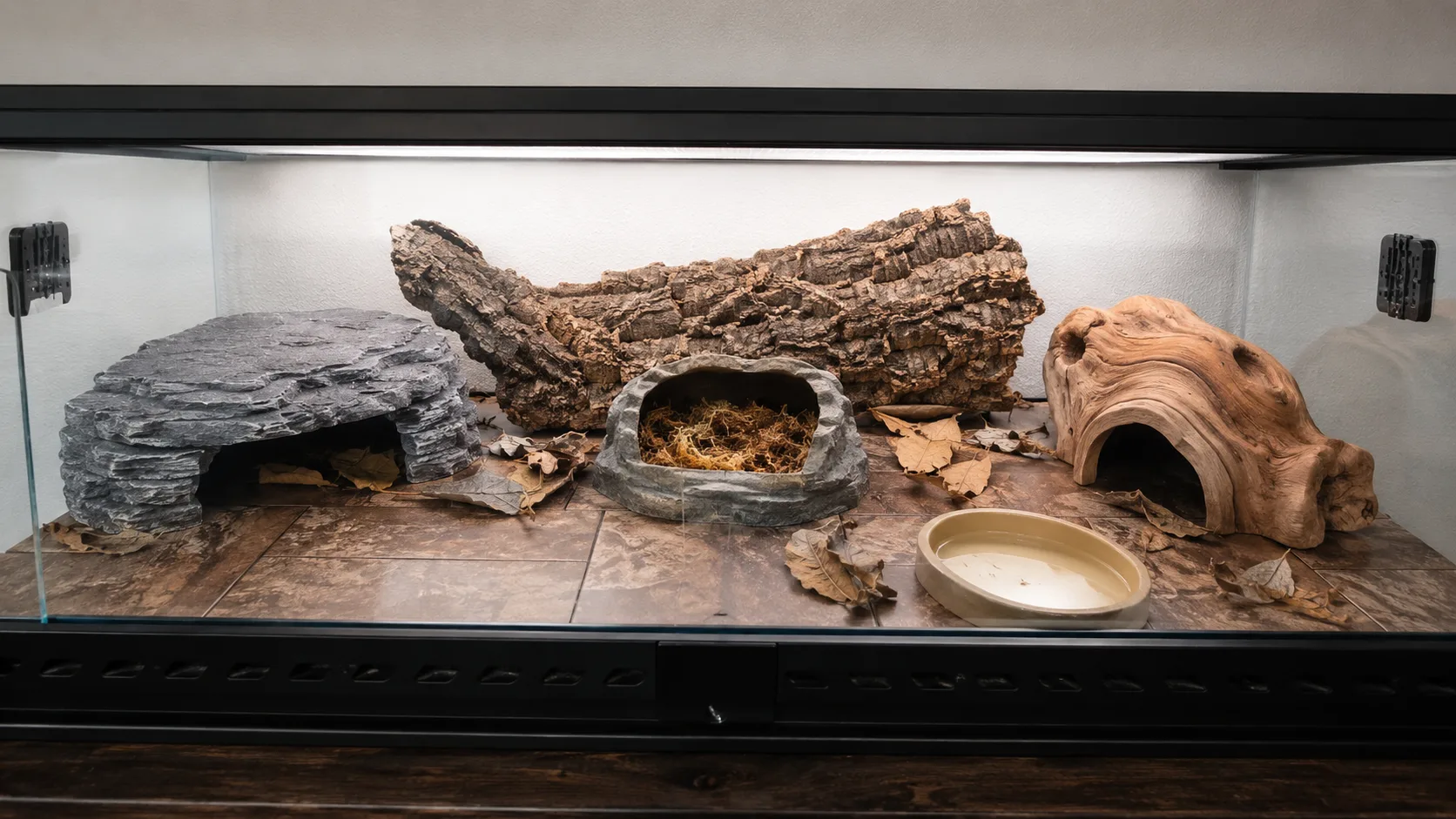 A well-furnished 36×18×18 in leopard gecko terrarium with three hides, slate basking ledge, water dish and cork bark décor on a tile substrate.